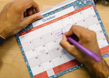 A hand writing dates on an October wall planner