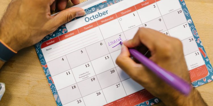 A hand writing dates on an October wall planner
