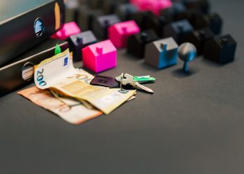 Miniature houses, euro bills, and a house key symbolize real estate investment and property transactions.