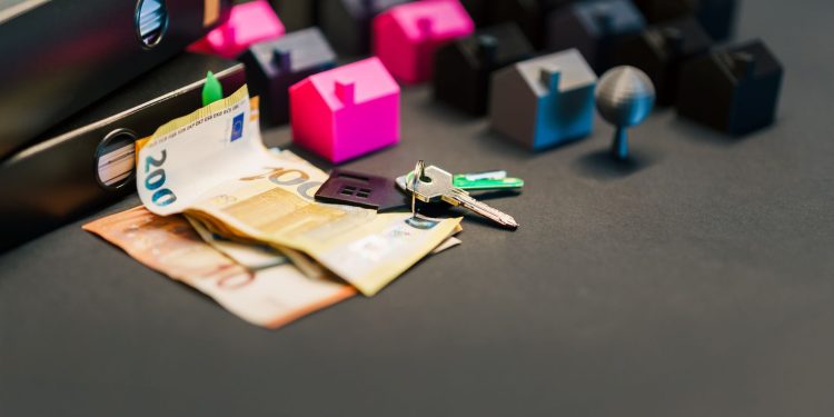 Miniature houses, euro bills, and a house key symbolize real estate investment and property transactions.