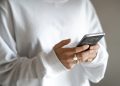 Households under pressure can move from impulse buys to planned repayments: a person in a white jumper checking their household budget on a mobile phone