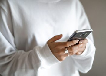 Households under pressure can move from impulse buys to planned repayments: a person in a white jumper checking their household budget on a mobile phone