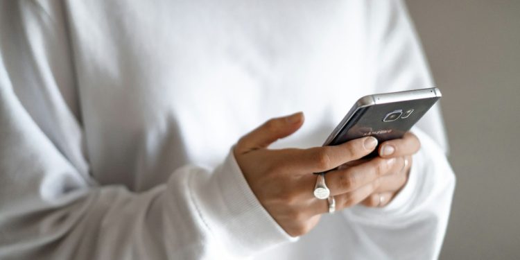 Households under pressure can move from impulse buys to planned repayments: a person in a white jumper checking their household budget on a mobile phone